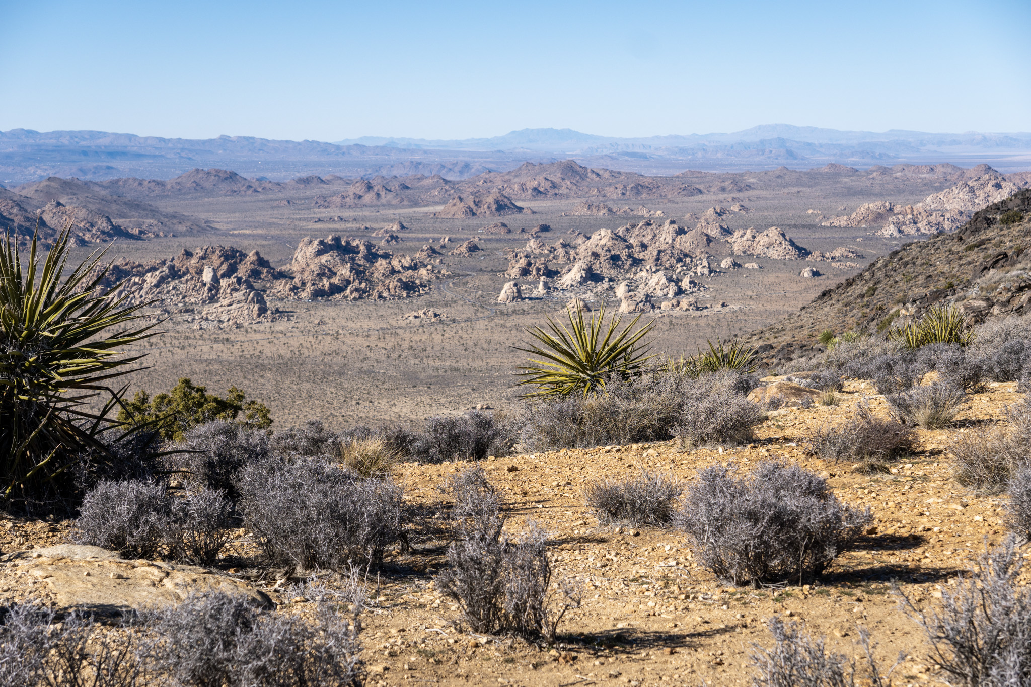 A view down into the Park from a rocky, desert peak, looking at the scabrous valley floor below. The sun beats down on it all.