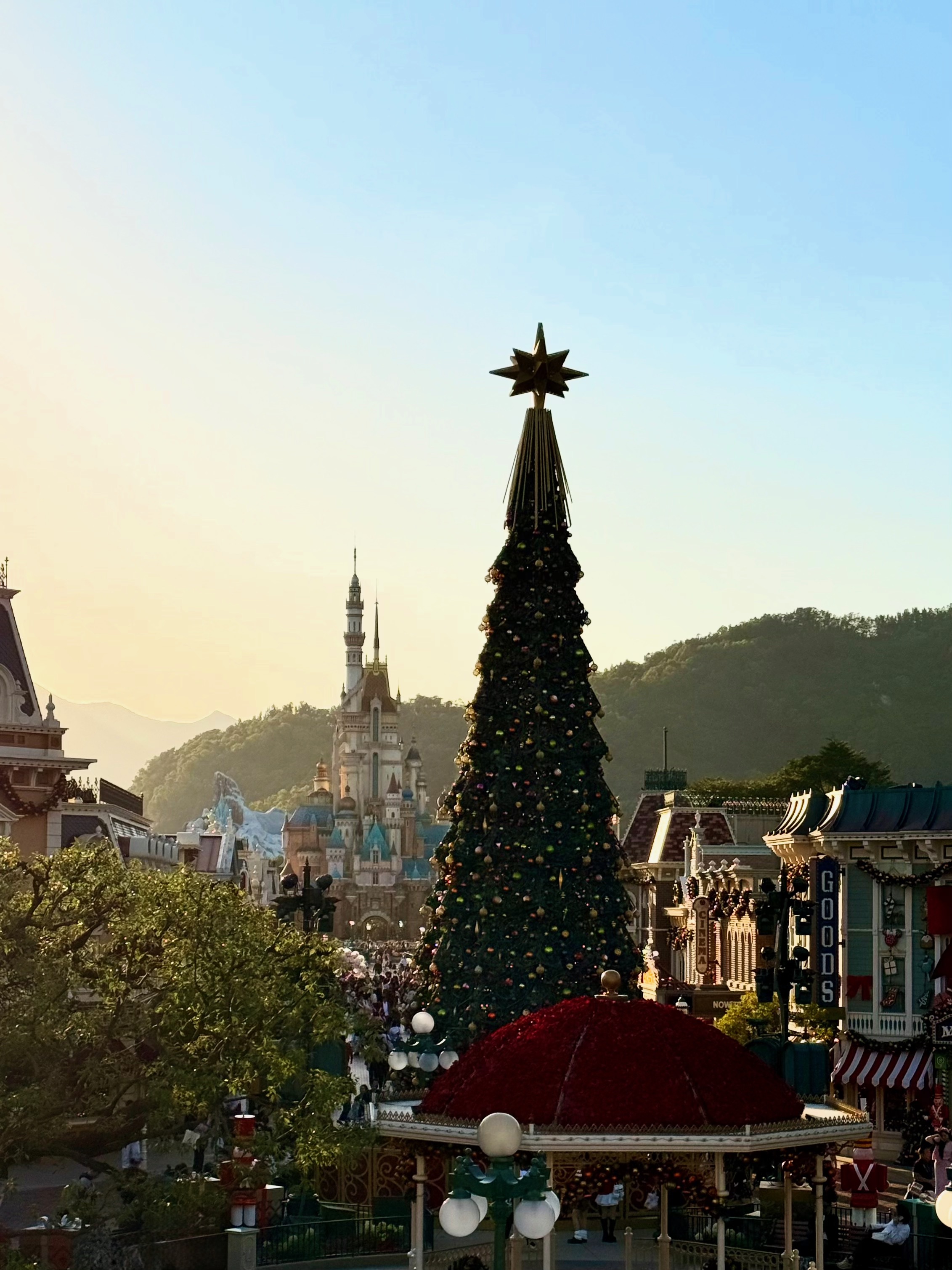 A photo of Hong Kong Disneyland's Main Street with their very large Christmas Tree and the castle in the distance at sunset.